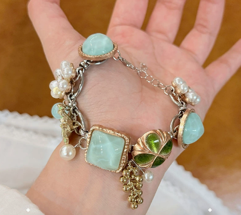Statement bracelet with aqua-colored stones, a green four-petal flower, pearly bead clusters and dangling charms.
