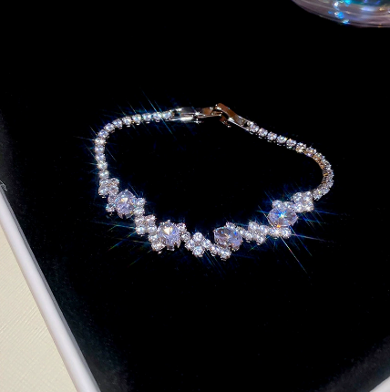26 - Silver Tone / Clear tennis bracelet with center stones, small clear geometric clusters and a clasp.