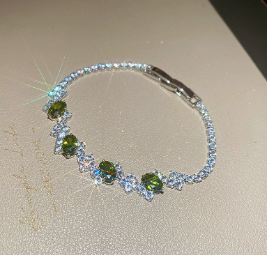 28 - Silver Tone / Olive Green tennis bracelet with center stones, small clear geometric clusters and a clasp.