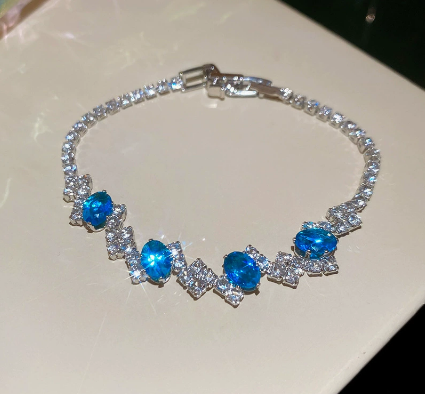 48 - Silver Tone / Blue tennis bracelet with center stones, small clear geometric clusters and a clasp.