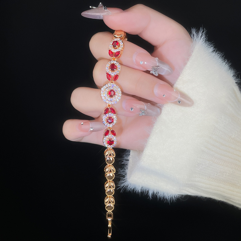 Gold-tone bracelet with red round center stones, clear halo accents and leaf-like links.