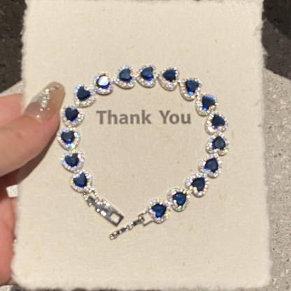Silver-tone bracelet with repeating dark blue heart-shaped stones bordered by clear accents.