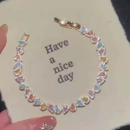 Silver-tone bracelet with repeating pastel-colored heart-shaped stones and clear halo accents.