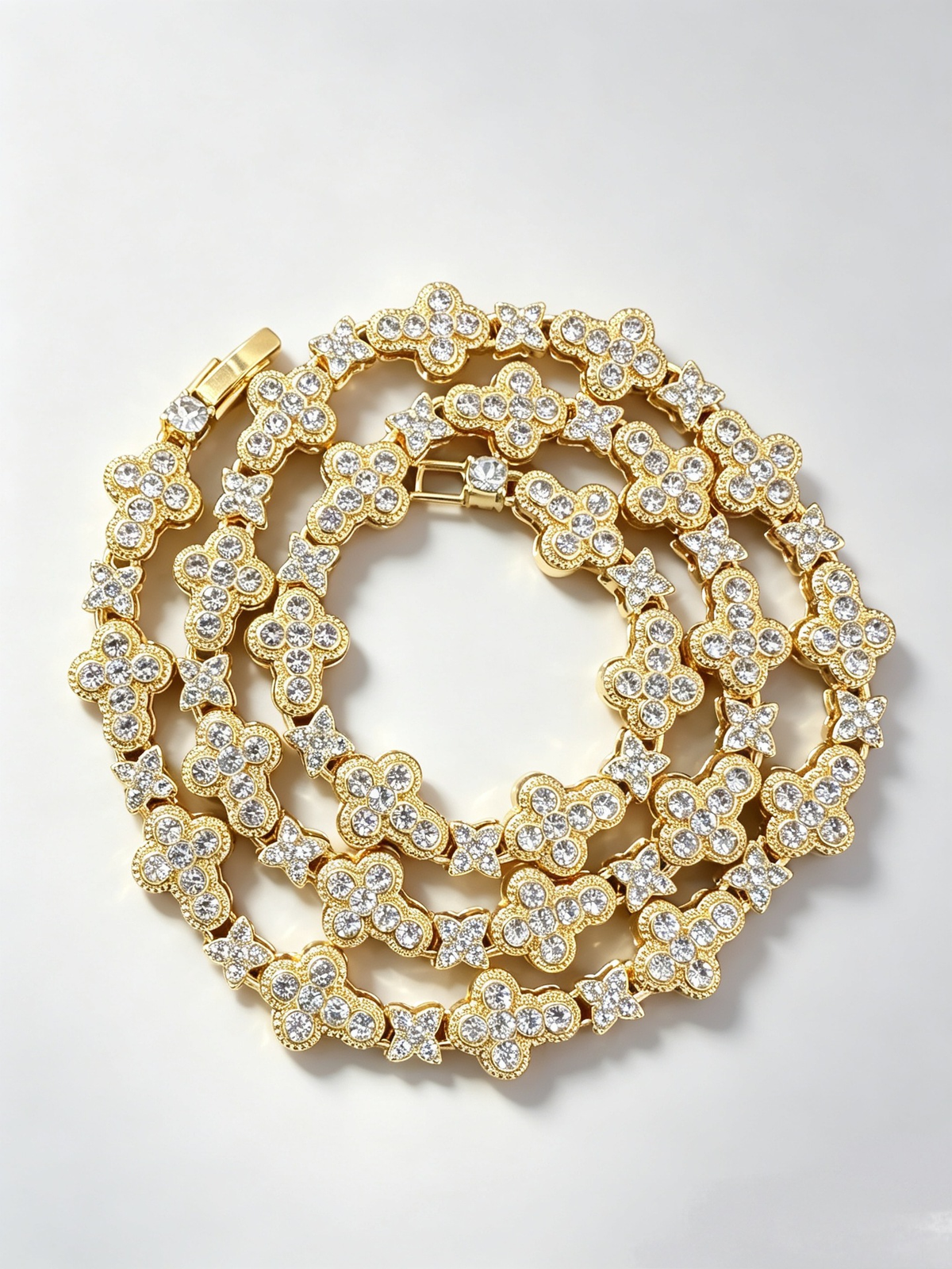 Gold-tone necklace with repeating rounded cross links, smaller four-petal motifs, clear stones and a clasp.